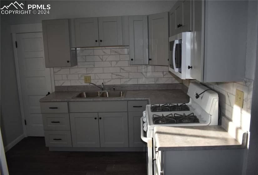 Kitchen with gray cabinets, dark wood-type flooring, tasteful backsplash, white range with gas stovetop, and sink