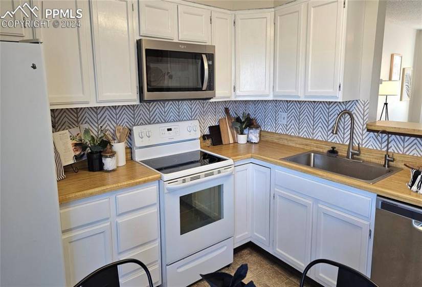 Kitchen with backsplash, white cabinets, sink, stainless steel appliances, and tile flooring