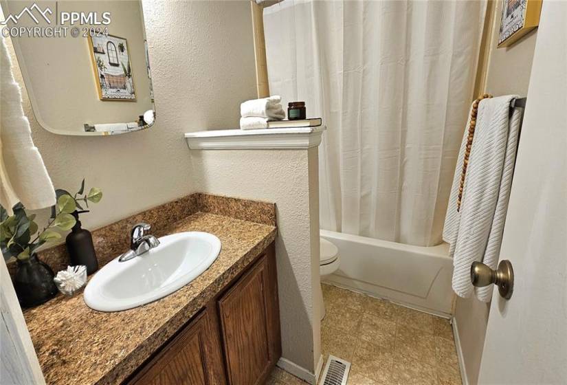 Full bathroom with vanity, toilet, shower / bath combo with shower curtain, and tile floors