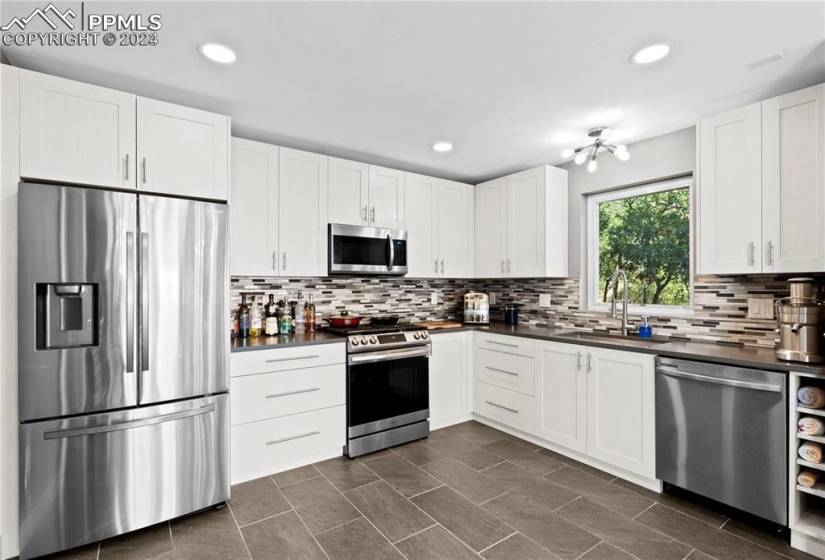 Kitchen with dark tile floors, white cabinetry, tasteful backsplash, appliances with stainless steel finishes, and sink
