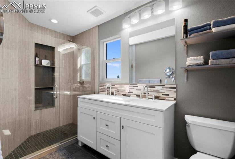 Bathroom with large vanity, toilet, a shower with shower door, tasteful backsplash, and tile flooring