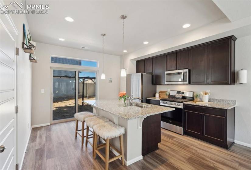 Kitchen featuring appliances with stainless steel finishes, sink, hanging light fixtures, dark brown cabinetry, and light wood-type flooring