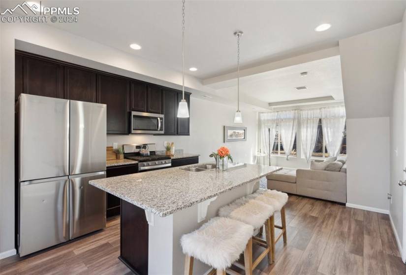 Kitchen featuring stainless steel appliances, an island with sink, light stone countertops, and hardwood / wood-style floors