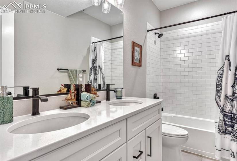 Full bathroom with dual sinks, shower / bath combo, oversized vanity, toilet, and tile floors