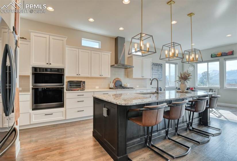 Kitchen featuring backsplash, wall chimney range hood, stainless steel appliances, light hardwood / wood-style flooring, and an island with sink