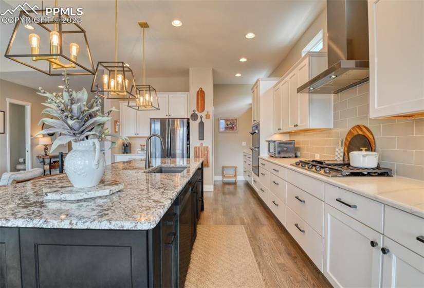 Kitchen featuring white cabinets, wall chimney range hood, light hardwood / wood-style floors, and a center island with sink