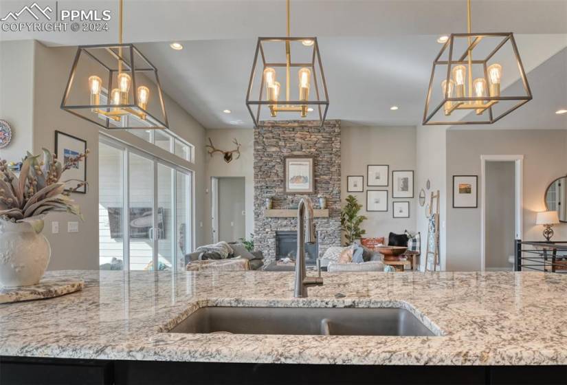 Kitchen featuring a notable chandelier, a fireplace, light stone counters, sink, and hanging light fixtures
