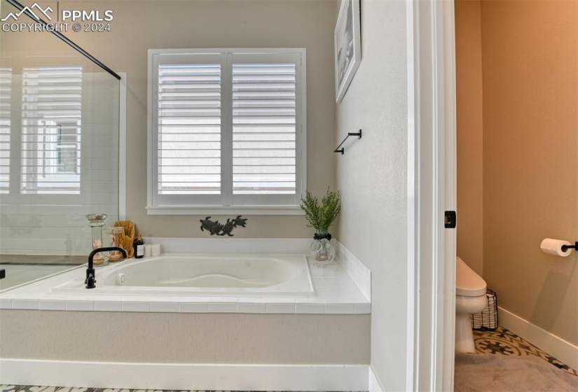 Bathroom with a wealth of natural light, tiled bath, toilet, and tile floors