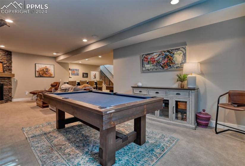 Rec room with light colored carpet, a stone fireplace, and pool table