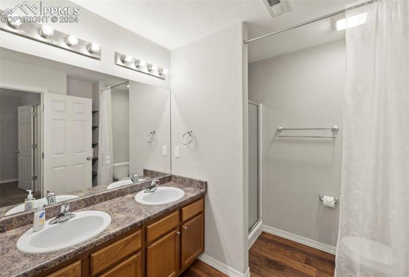Primary Bathroom with hardwood / wood-style floors, large vanity, dual sinks, and walk in shower