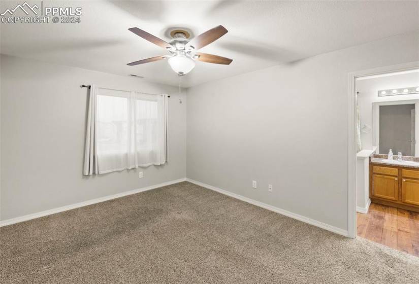 Carpeted primary bedroom with ceiling fan and attached bathroom