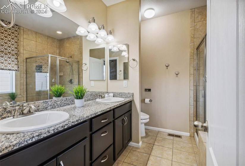 Bathroom featuring dual sinks, a shower with door, toilet, tile floors, and oversized vanity