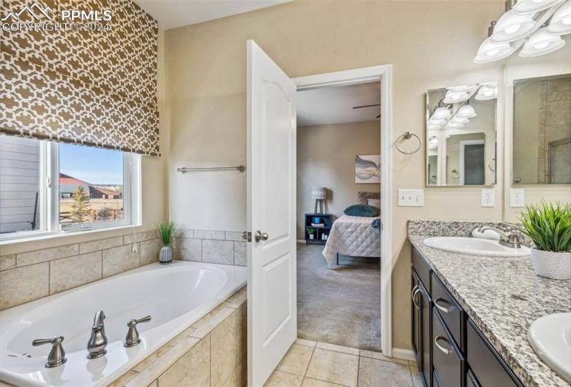 Bathroom with tile flooring, dual bowl vanity, and a relaxing tiled bath