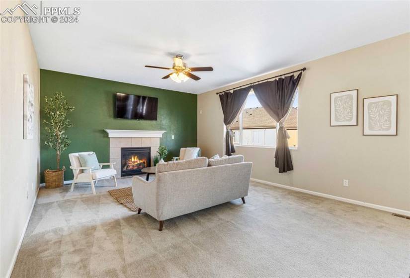 Living room with a tiled fireplace, light colored carpet, and ceiling fan