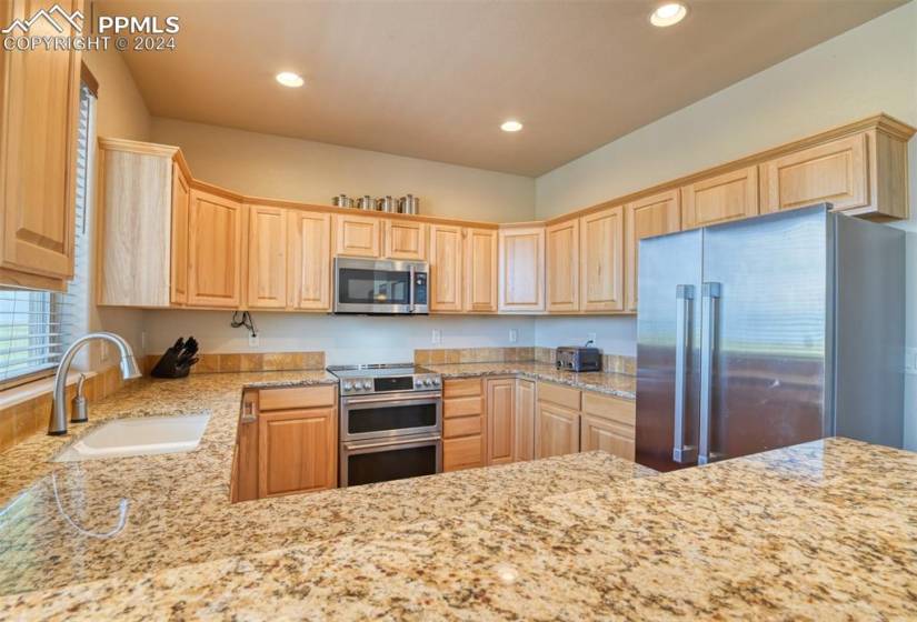 Kitchen with light stone counters, high quality appliances, light brown cabinetry, and sink