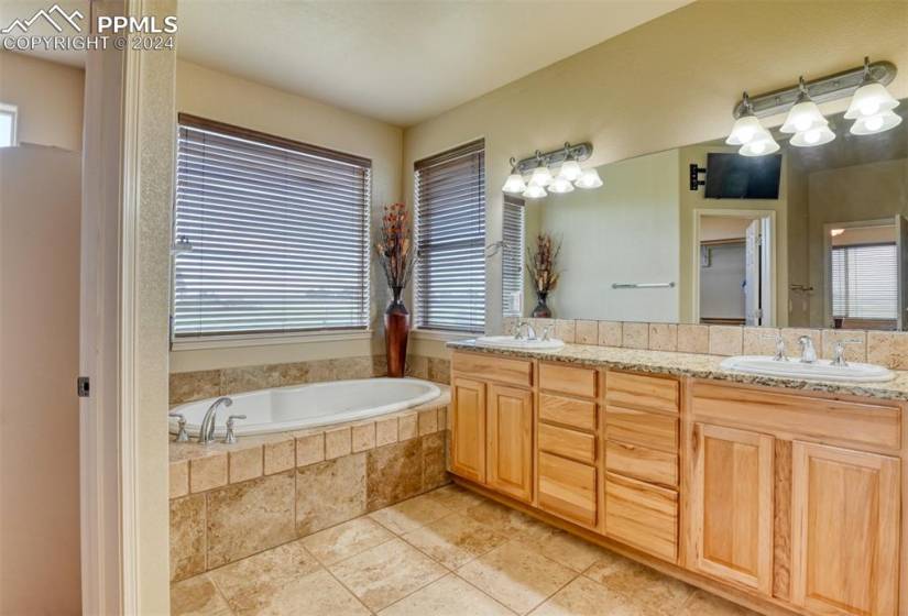 Bathroom featuring dual sinks, a relaxing tiled bath, oversized vanity, and tile flooring