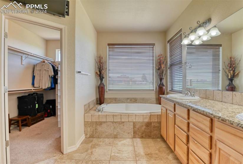 Bathroom with a relaxing tiled bath, vanity with extensive cabinet space, and tile flooring