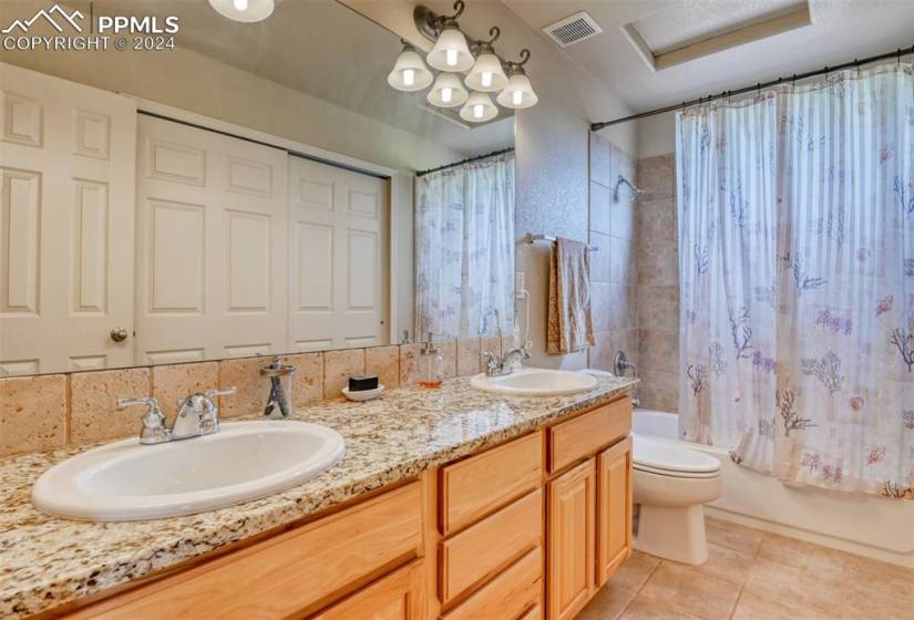 Full bathroom with shower / bath combo, toilet, tile flooring, double sink, and vanity with extensive cabinet space