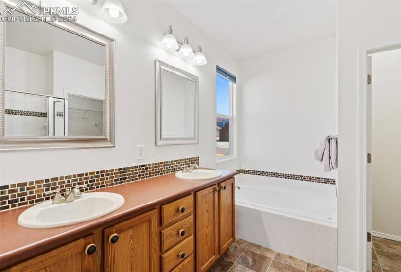 Bathroom with tiled tub, double vanity, tile floors, and tasteful backsplash