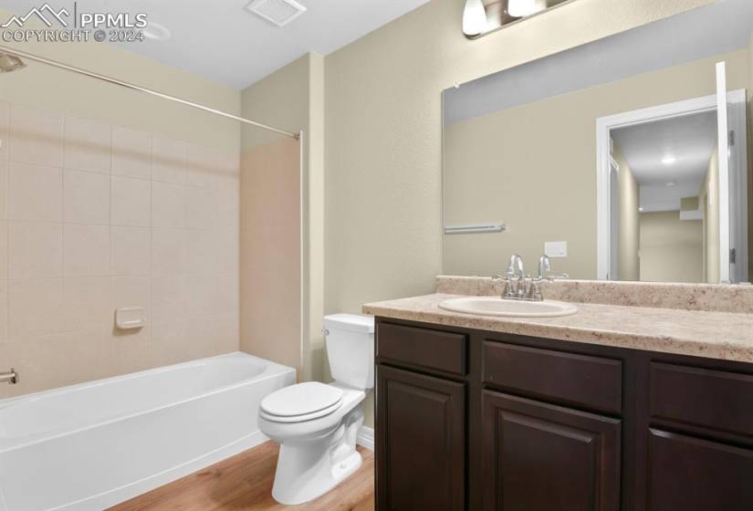 Full bathroom with toilet, tiled shower / bath, vanity with extensive cabinet space, and hardwood / wood-style floors