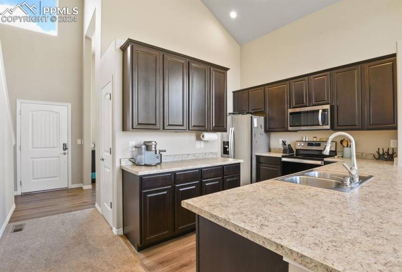 Kitchen featuring light luxury vinyl flooring, dark brown cabinets, stainless steel appliances, high vaulted ceiling, and sink