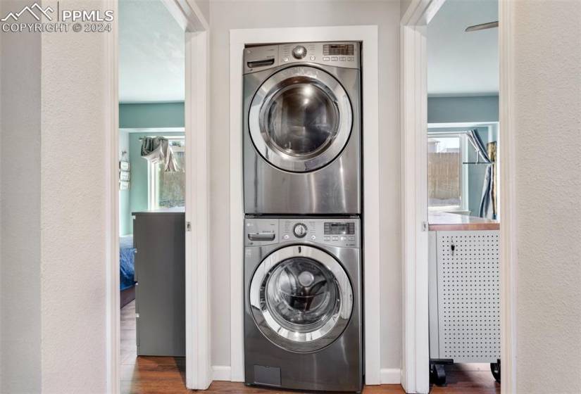 Laundry room with stacked washer and dryer and dark wood-type flooring