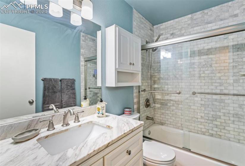 Full bathroom featuring shower / bath combination with glass door, toilet, and vanity with extensive cabinet space