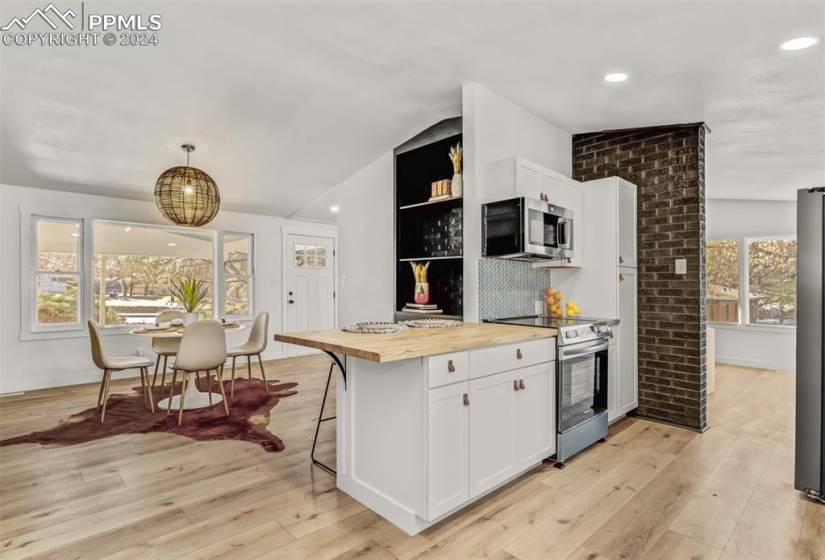 Kitchen with vaulted ceiling, appliances with stainless steel finishes, white cabinetry, light wood-type flooring, and butcher block counters. Wonderful natural light