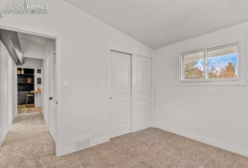 Unfurnished bedroom featuring light colored carpet, vaulted ceiling, and a closet