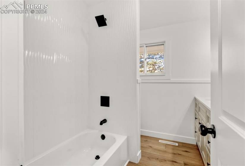 Bathroom with shower / tub combination, gorgeous wrap around designer tile, hardwood / wood-style floors, and vanity