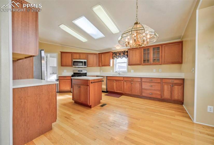 Kitchen featuring appliances with stainless steel finishes, a chandelier, lofted ceiling, hanging light fixtures, and light hardwood / wood-style flooring
