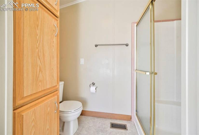 Bathroom with toilet, a shower with door, and tile flooring