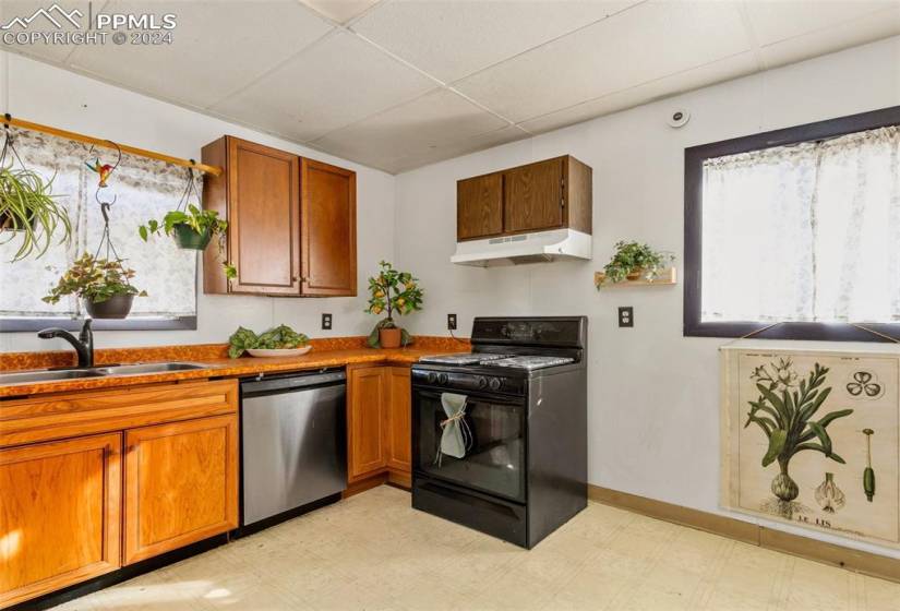 Kitchen with a drop ceiling, sink, light tile floors, stainless steel dishwasher, and black range with gas stovetop