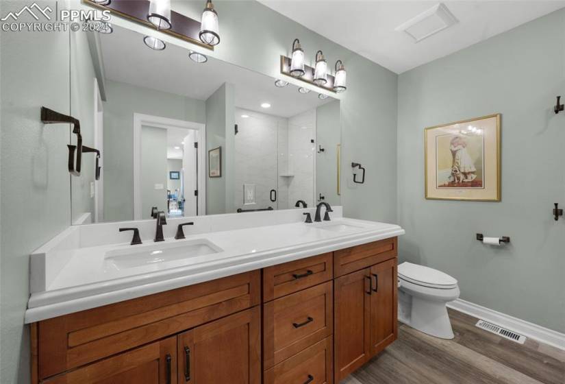 Bathroom featuring double vanity, a shower with shower door, wood-type flooring, and toilet