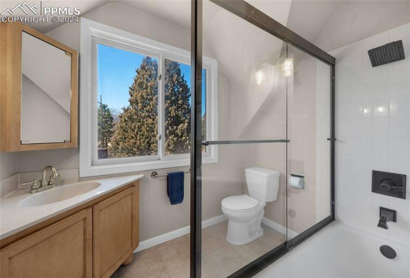 Full bathroom with toilet, plenty of natural light, vaulted ceiling, and tile floors