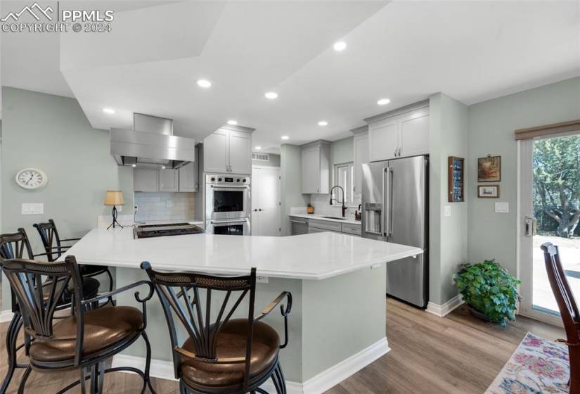Kitchen featuring tasteful backsplash, wall chimney exhaust hood, appliances with stainless steel finishes, light hardwood / wood-style flooring, and a kitchen breakfast bar