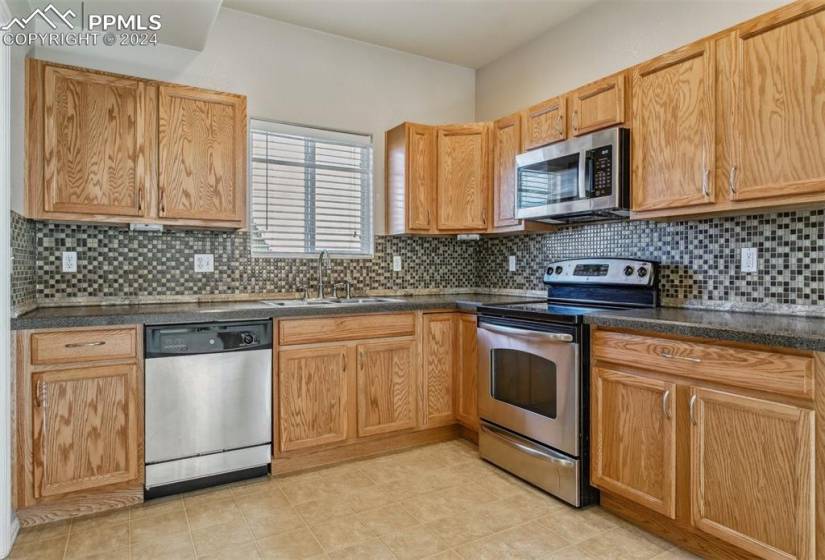 Kitchen with appliances with stainless steel finishes, light tile flooring, sink, and tasteful backsplash