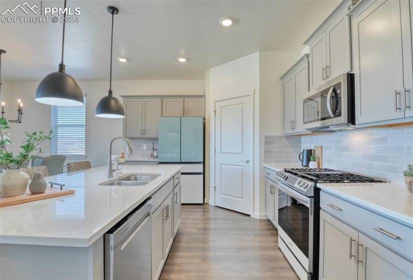 Kitchen featuring tasteful backsplash, hanging light fixtures, an island with sink, wood-type flooring, and stainless steel appliances