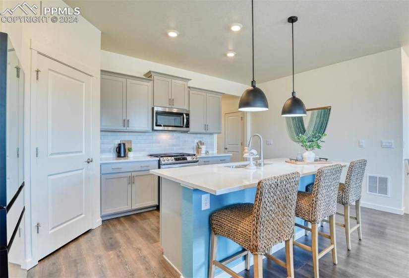 Kitchen featuring appliances with stainless steel finishes, a kitchen island with sink, sink, light hardwood / wood-style flooring, and pendant lighting