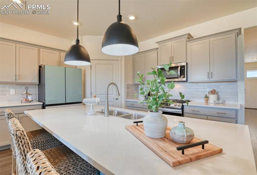 Kitchen with backsplash, appliances with stainless steel finishes, a kitchen island with sink, pendant lighting, and gray cabinets