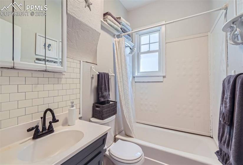Full bathroom with tile walls, shower / bath combo with shower curtain, toilet, and vanity