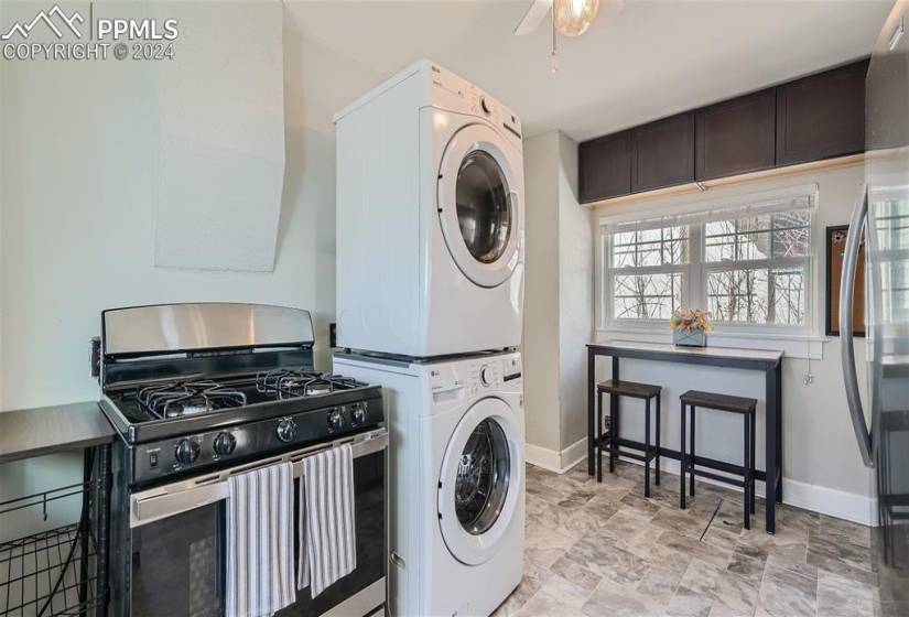 Laundry area featuring stacked washer / dryer, light tile floors, and ceiling fan