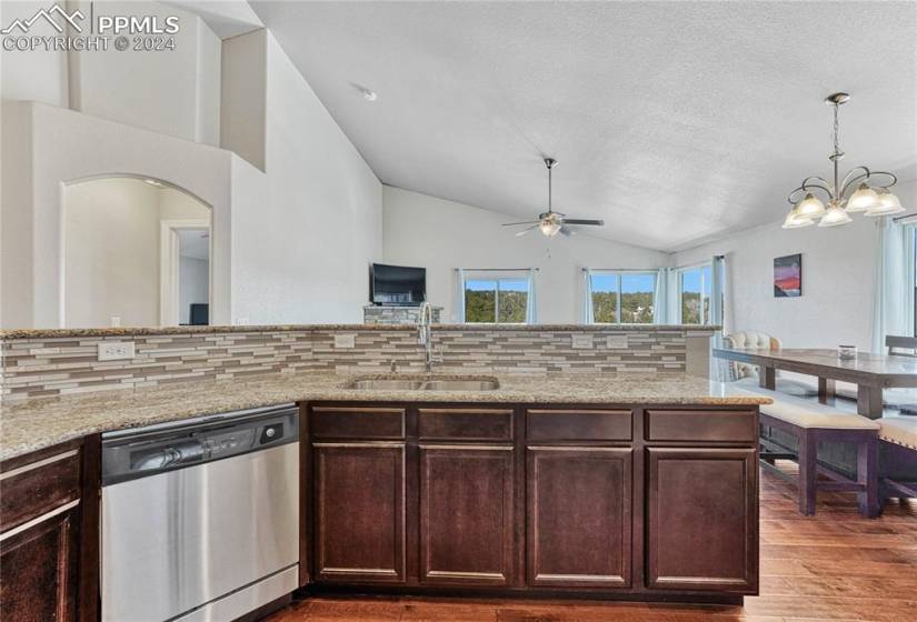 Kitchen featuring backsplash, vaulted ceiling, stainless steel dishwasher, sink, and ceiling fan with notable chandelier