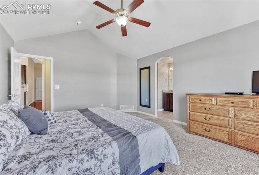 Carpeted bedroom with high vaulted ceiling, ensuite bathroom, and ceiling fan