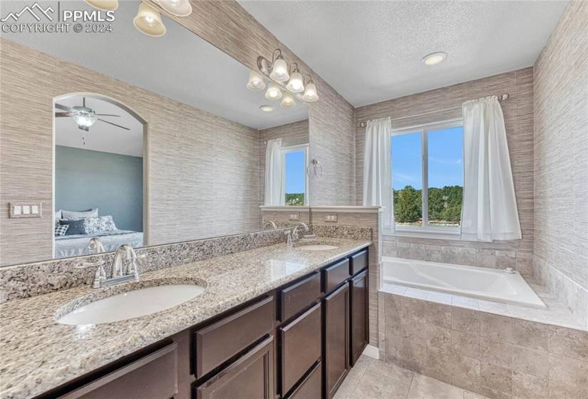 Bathroom with ceiling fan, vanity with extensive cabinet space, a relaxing tiled bath, tile flooring, and double sink