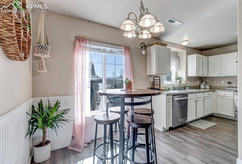 Kitchen featuring a charming chandelier, a wealth of natural light, white cabinetry, and stainless steel dishwasher