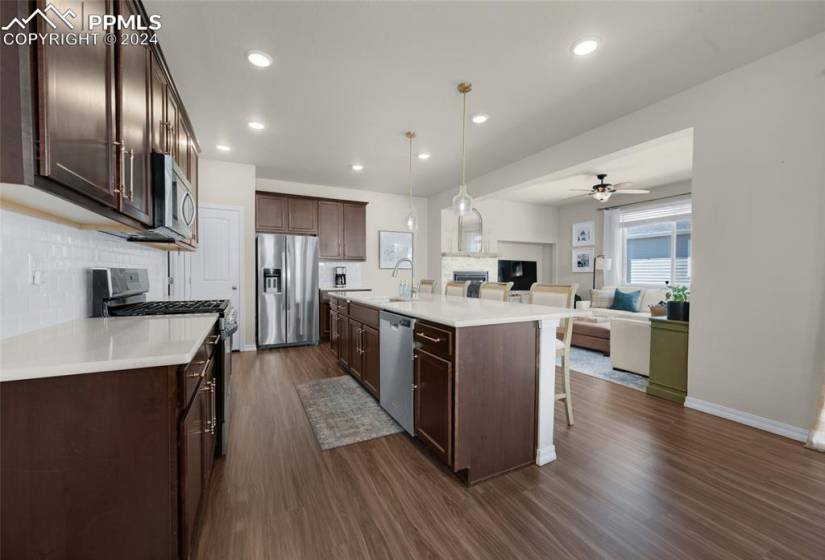 Kitchen with ceiling fan, dark wood-type flooring, a kitchen breakfast bar, hanging light fixtures, and stainless steel appliances