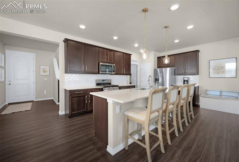 Kitchen with dark hardwood / wood-style floors, a breakfast bar, tasteful backsplash, hanging light fixtures, and appliances with stainless steel finishes