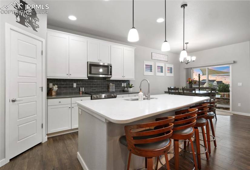 Kitchen with dark wood-type flooring, hanging light fixtures, a center island with sink, and a breakfast bar area