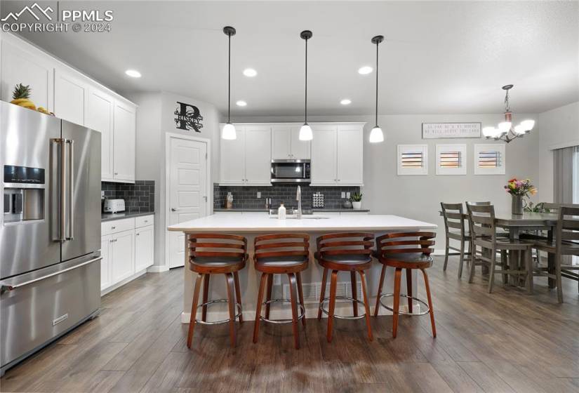 Kitchen with pendant lighting, stainless steel appliances, an island with sink, and dark wood-type flooring